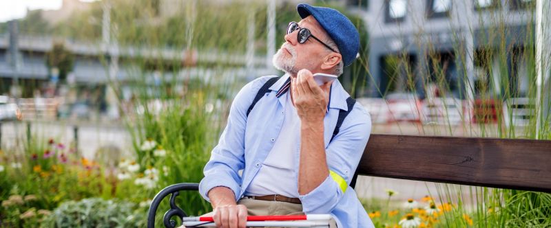Mann sitzt auf einer Parkbank mit einem Blindenstock in der Hand