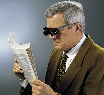 Mann liest mit einer Fernrohrbrille die Zeitung